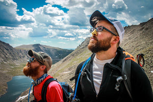 Two men on a hike wearing Nöz brand sunscreen called Nözscreen. Made of organic, reef safe minerals, they are looking cool, wearing colors yellow and blue that represents their individual personalities while protecting their skin and the environment.